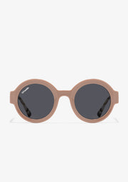 Round-rimmed sunglasses with shiny tan frame and smoke-colored lenses, featuring a logo on the temples and an emblem on the lens.